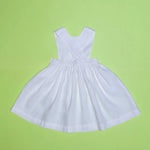 Vista de costas do vestido infantil de linho branco com alças cruzadas e saia ampla, em superfície verde.