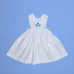 Vestido infantil de linho branco com bordado à mão de conchas azuis para meninas, visto de frente em superfície azul.