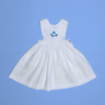 Vestido infantil de linho branco com bordado à mão de conchas azuis para meninas, visto de frente em superfície azul.