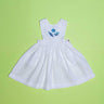 Vestido infantil de linho branco com bordado à mão de conchas azuis para meninas, visto de frente em superfície verde.