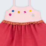 Vestido infantil em linho cereja e rosa com flores bordadas à mão e detalhe franzido na cintura, visto de frente em detalhe.