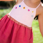 Menina usando vestido infantil em linho cereja e rosa com bordado de flores coloridas e franzido na cintura.