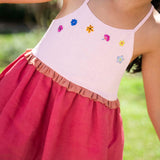 Menina usando vestido infantil em linho cereja e rosa com bordado de flores coloridas e franzido na cintura.