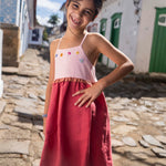 Menina usando vestido infantil em linho cereja e rosa com bordado de flores coloridas.