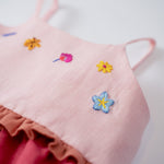 Detalhe das flores bordadas à mão no busto do vestido infantil em linho rosa e cereja.