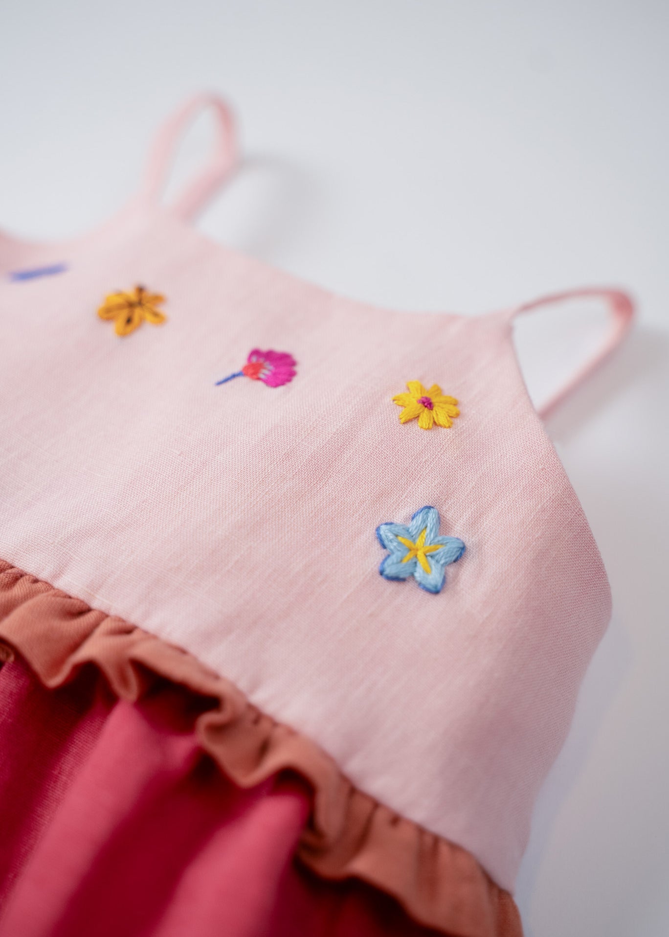 Detalhe das flores bordadas à mão no busto do vestido infantil em linho rosa e cereja.