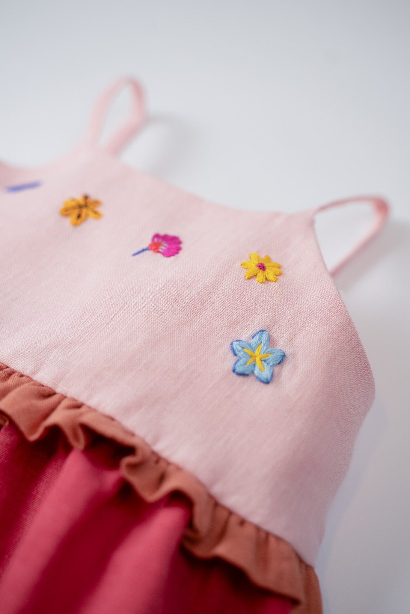 Detalhe das flores bordadas à mão no busto do vestido infantil em linho rosa e cereja.