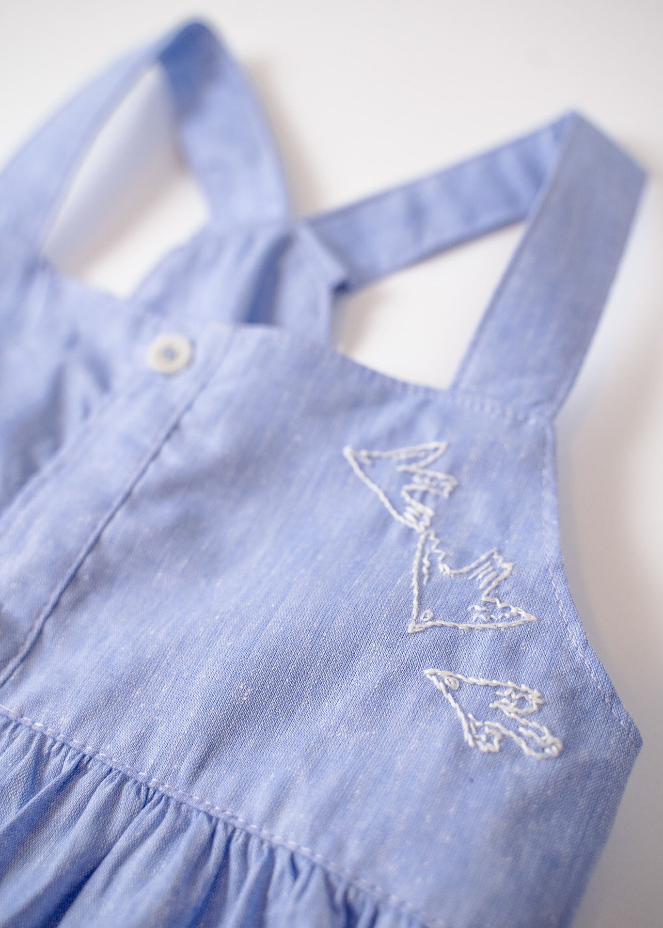 Detalhe do bordado de pássaros do vestido infantil em linho e algodão azul.