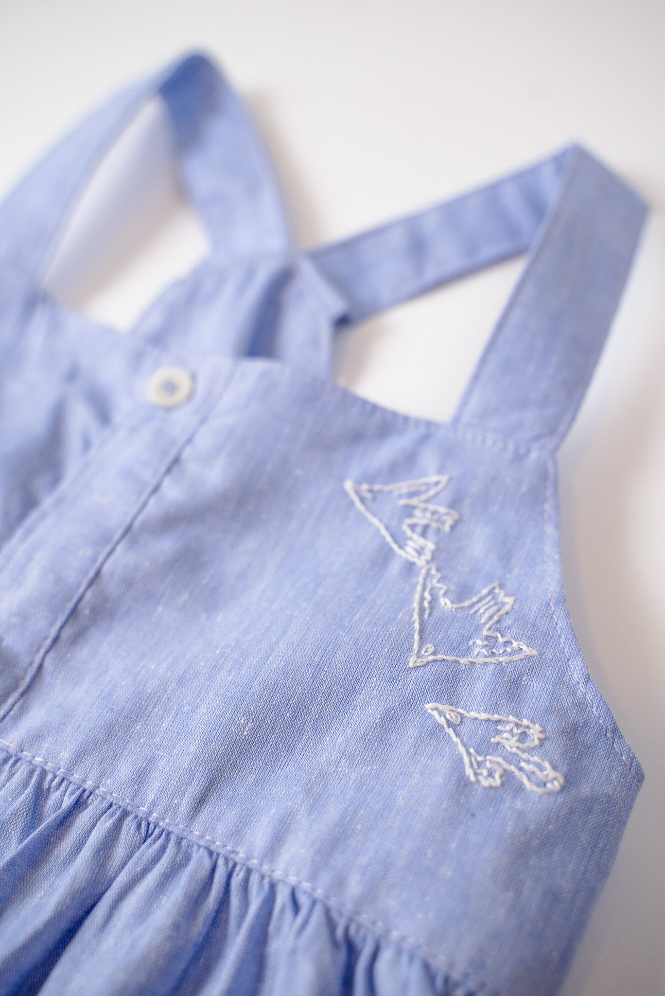 Detalhe do bordado de pássaros do vestido infantil em linho e algodão azul.