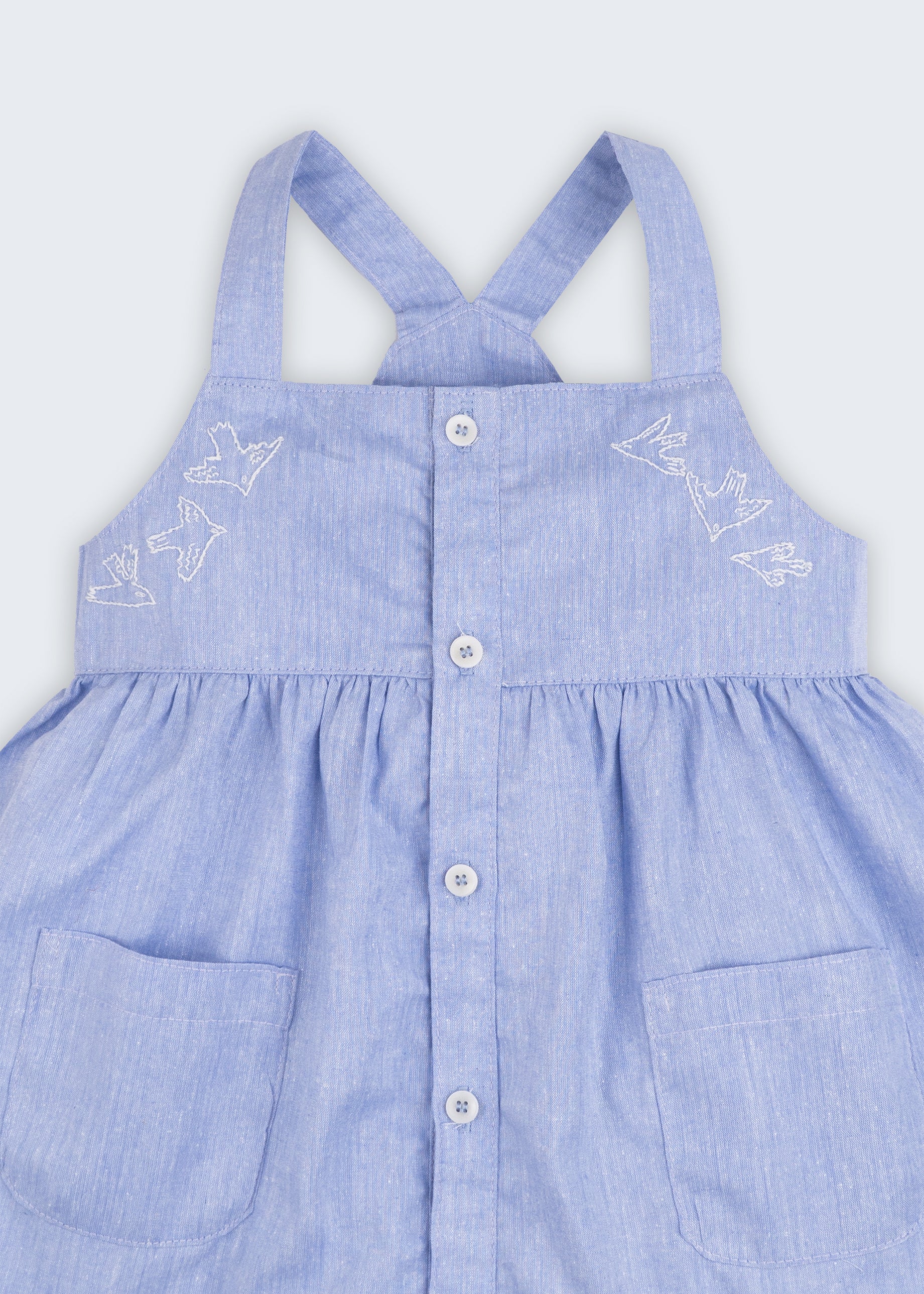 Vestido azul em linho e algodão infantil com pássaros bordados à mão para meninas, visto em detalhe.