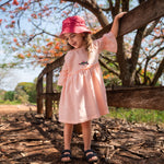 Menina usando vestido Pietra em puro linho rosa claro, com mangas e saia com babado.
