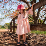 Menina usando vestido Pietra em puro linho rosa claro, com mangas e saia com babado.