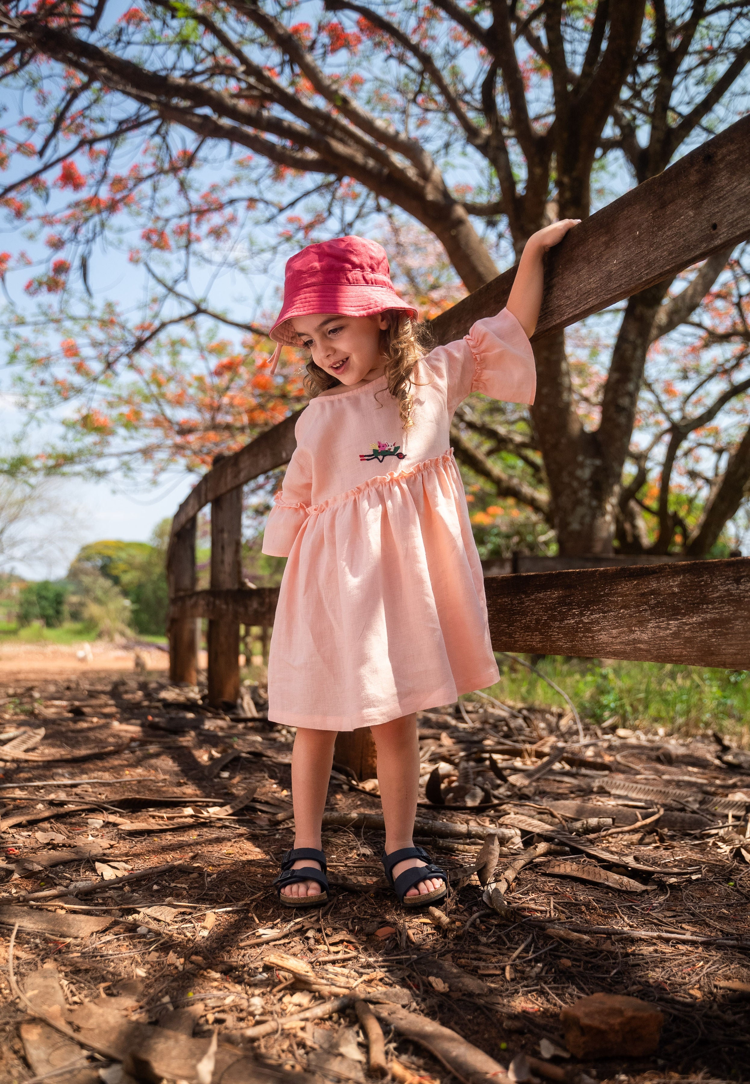 Menina usando vestido Pietra em puro linho rosa claro, com mangas e saia com babado.