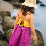 Costas do vestido infantil em linho roxo e amarelo com amarração ajustável e detalhe franzido verde, em look de verão.