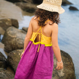 Costas do vestido infantil em linho roxo e amarelo com amarração ajustável e detalhe franzido verde, em look de verão.