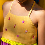 Close de menina com vestido infantil em linho roxo com alças finas e pala amarela com mini bordados manuais de bichinhos do fundo do mar, como polvo e cavalo-marinho.