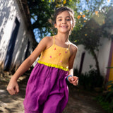 Menina usando vestido infantil em linho roxo e amarelo com bordados manuais na pala de conchas, estrelas do mar, polvo e cavalo-marinho.