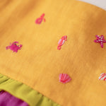 Close nos bordados manuais de bichinhos marinhos em vestido infantil para meninas de linho amarelo e roxo.