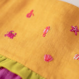 Close nos bordados manuais de bichinhos marinhos em vestido infantil para meninas de linho amarelo e roxo.