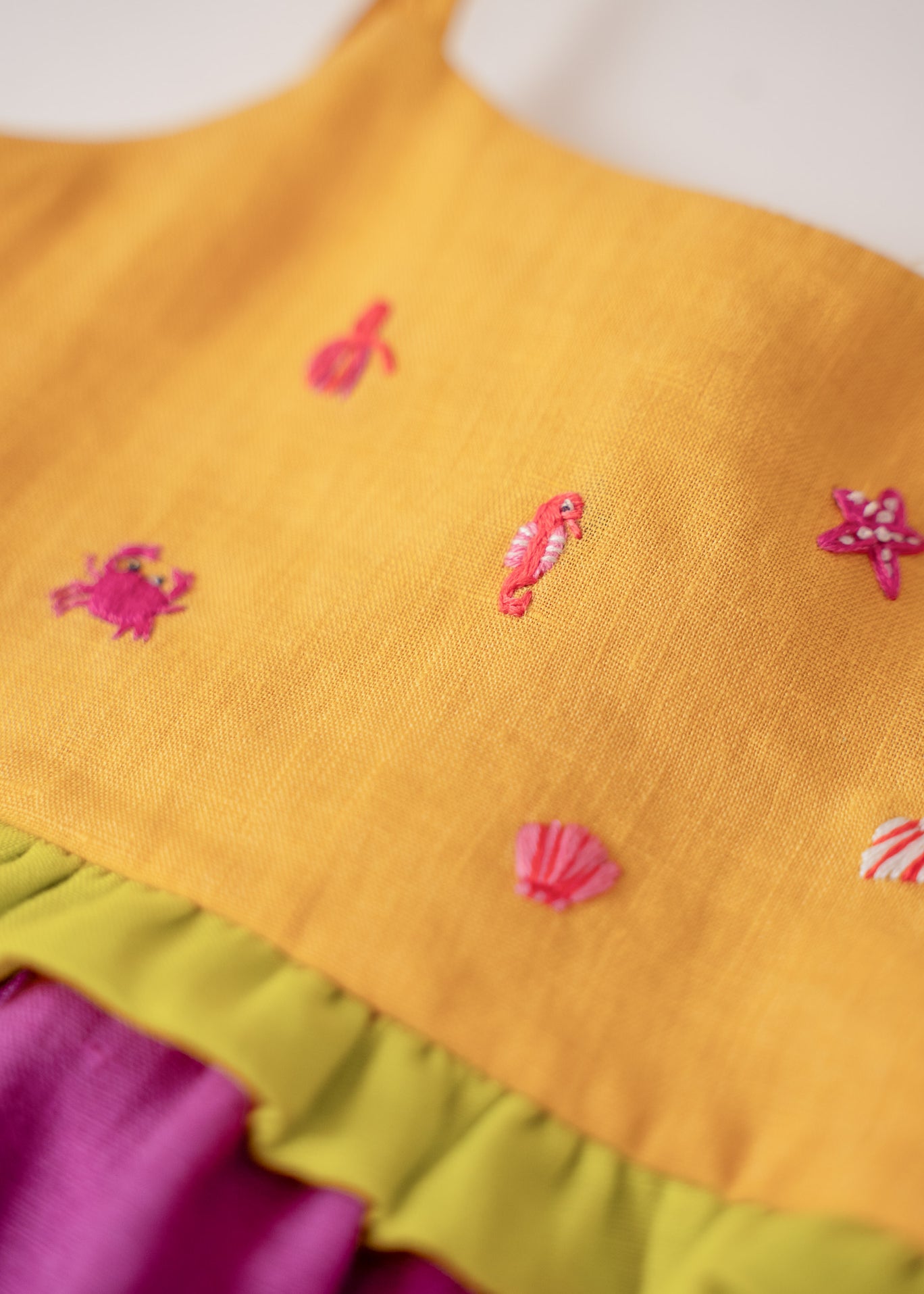 Close nos bordados manuais de bichinhos marinhos em vestido infantil para meninas de linho amarelo e roxo.