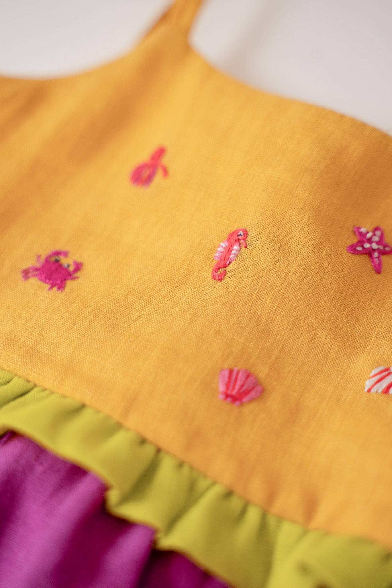 Close nos bordados manuais de bichinhos marinhos em vestido infantil para meninas de linho amarelo e roxo.