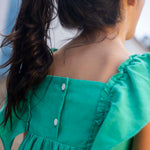 Vista das costas de menina com vestido infantil em linho verde-água com fechamento em botões brancos.