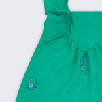 Vestido infantil em linho verde-água com bordado à mão de conchas e estrelas, visto de frente em detalhe.