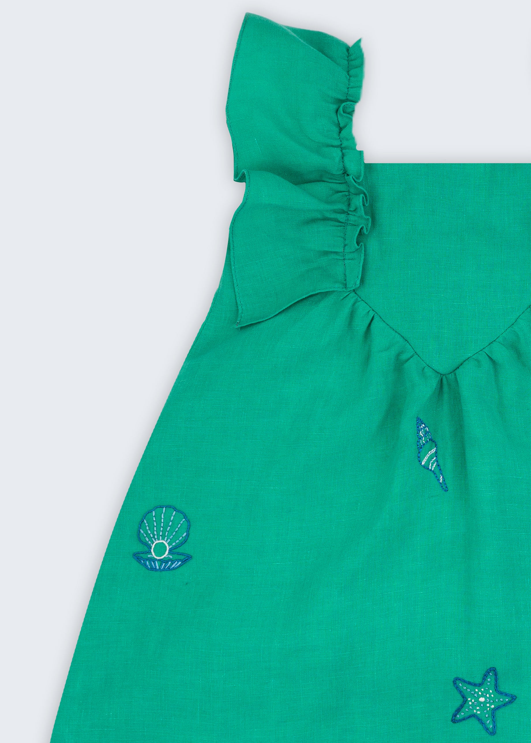Vestido infantil em linho verde-água com bordado à mão de conchas e estrelas, visto de frente em detalhe.