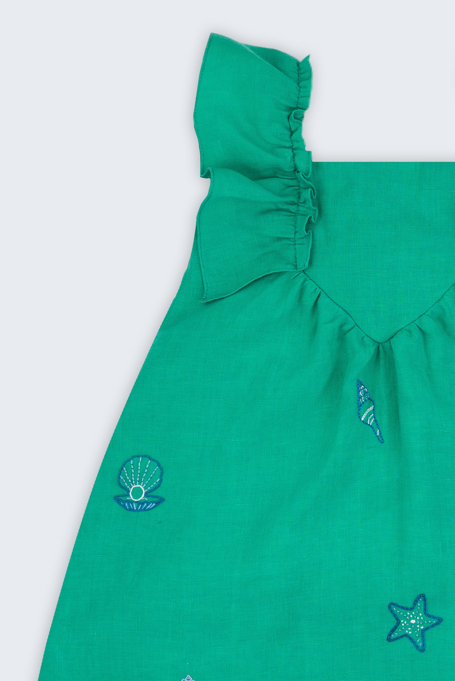 Vestido infantil em linho verde-água com bordado à mão de conchas e estrelas, visto de frente em detalhe.