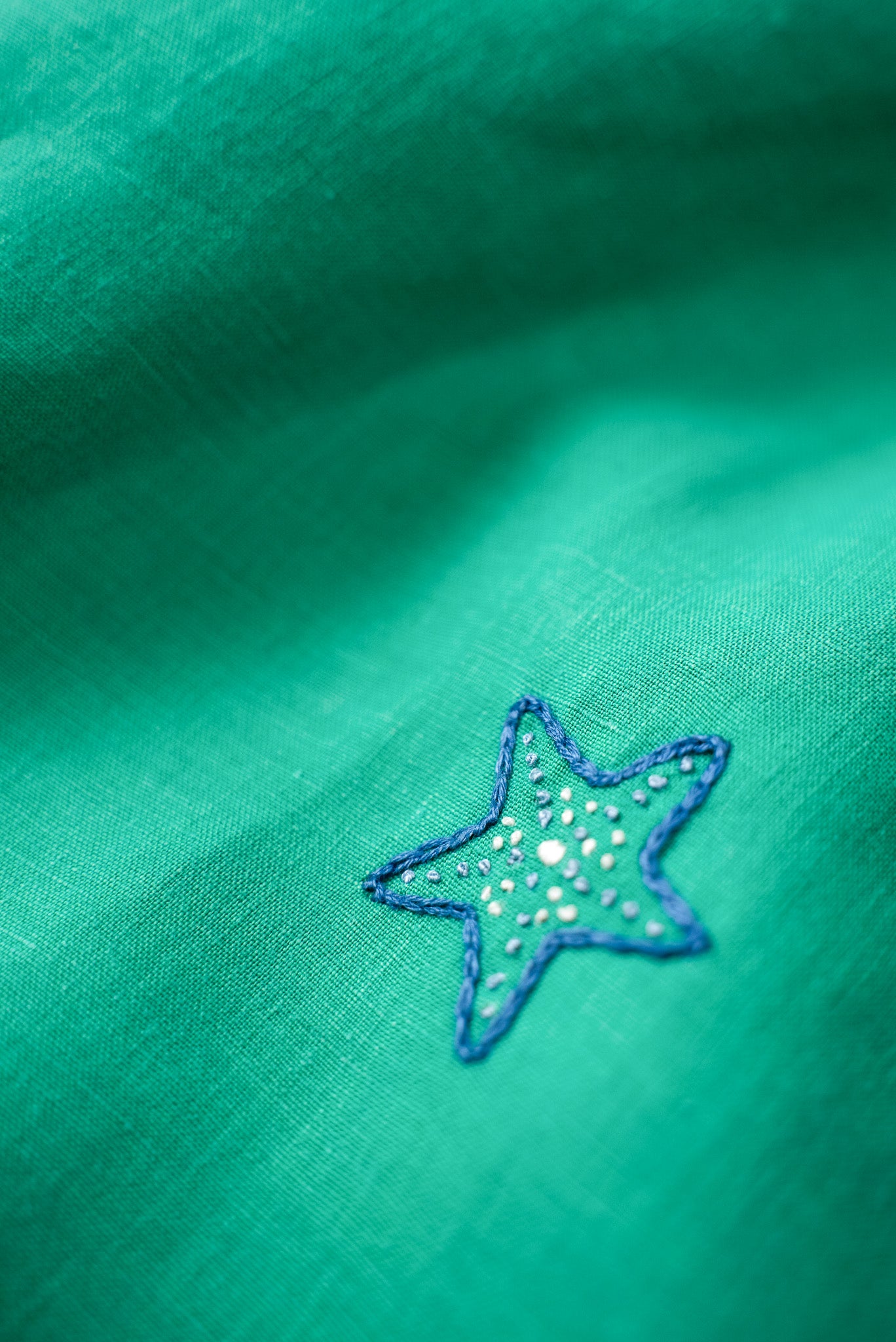 Detalhe do bordado à mão de estrela-do-mar no vestido infantil em linho verde-água.