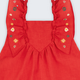 Vestido infantil em linho vermelho com babados e bordado à mão de estrelas natalinas nas alças, visto de frente em detalhe.