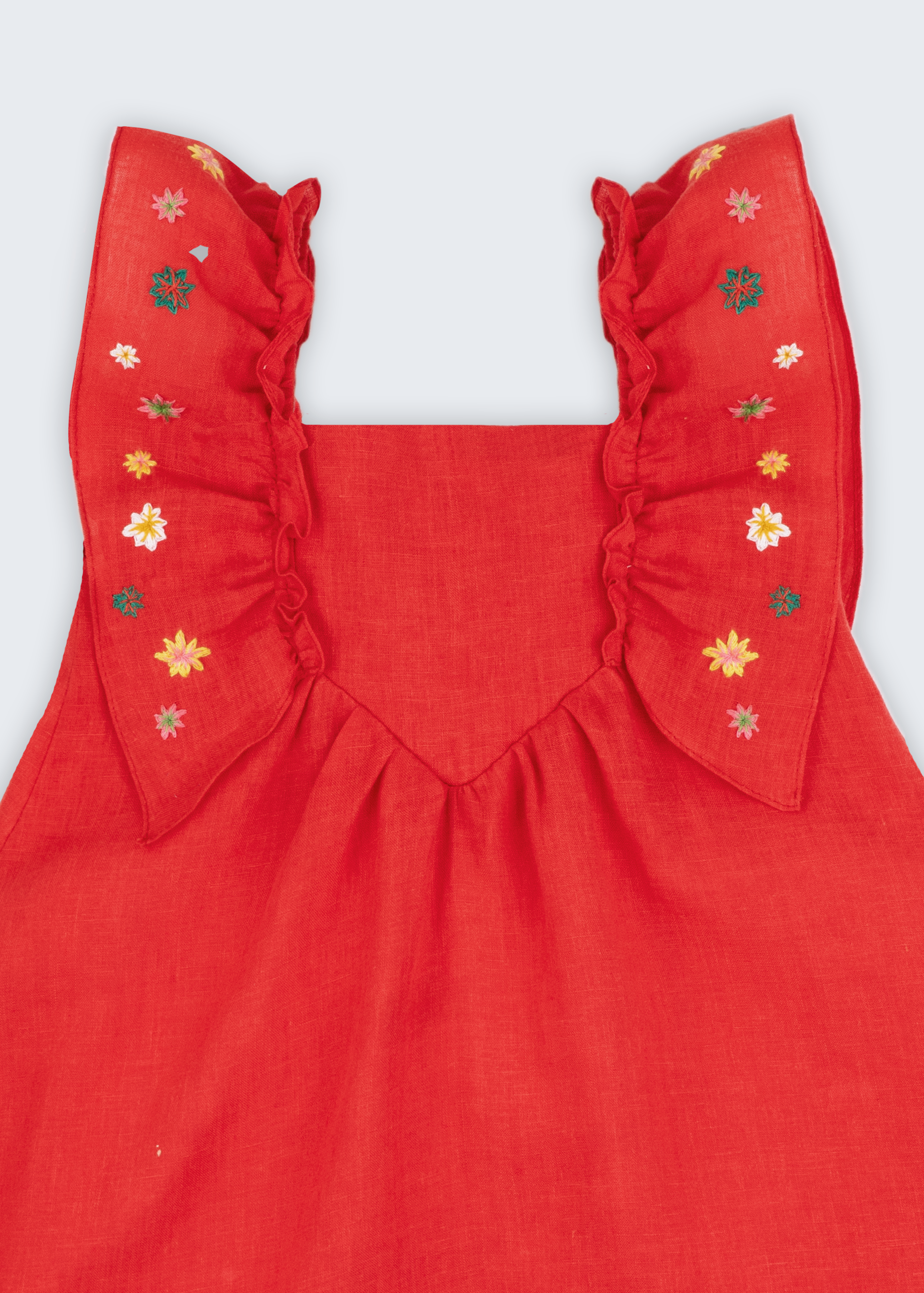 Vestido infantil em linho vermelho com babados e bordado à mão de estrelas natalinas nas alças, visto de frente em detalhe.