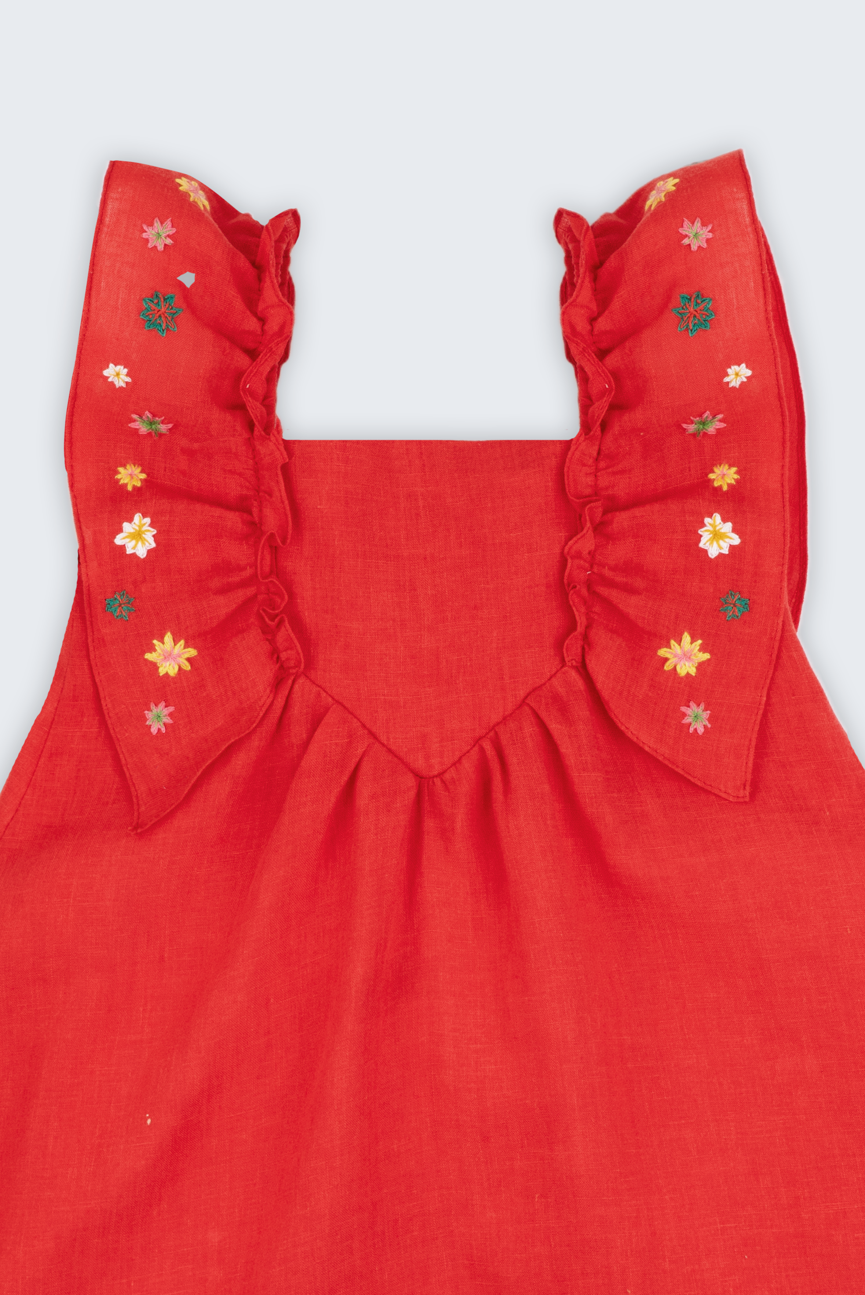 Vestido infantil em linho vermelho com babados e bordado à mão de estrelas natalinas nas alças, visto de frente em detalhe.