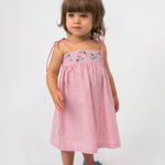 Menina vestindo Vestido Flora vermelho listrado, com flores bordadas à mão e alças de amarrar nos ombros.