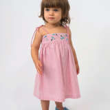Menina vestindo Vestido Flora vermelho listrado, com flores bordadas à mão e alças de amarrar nos ombros.