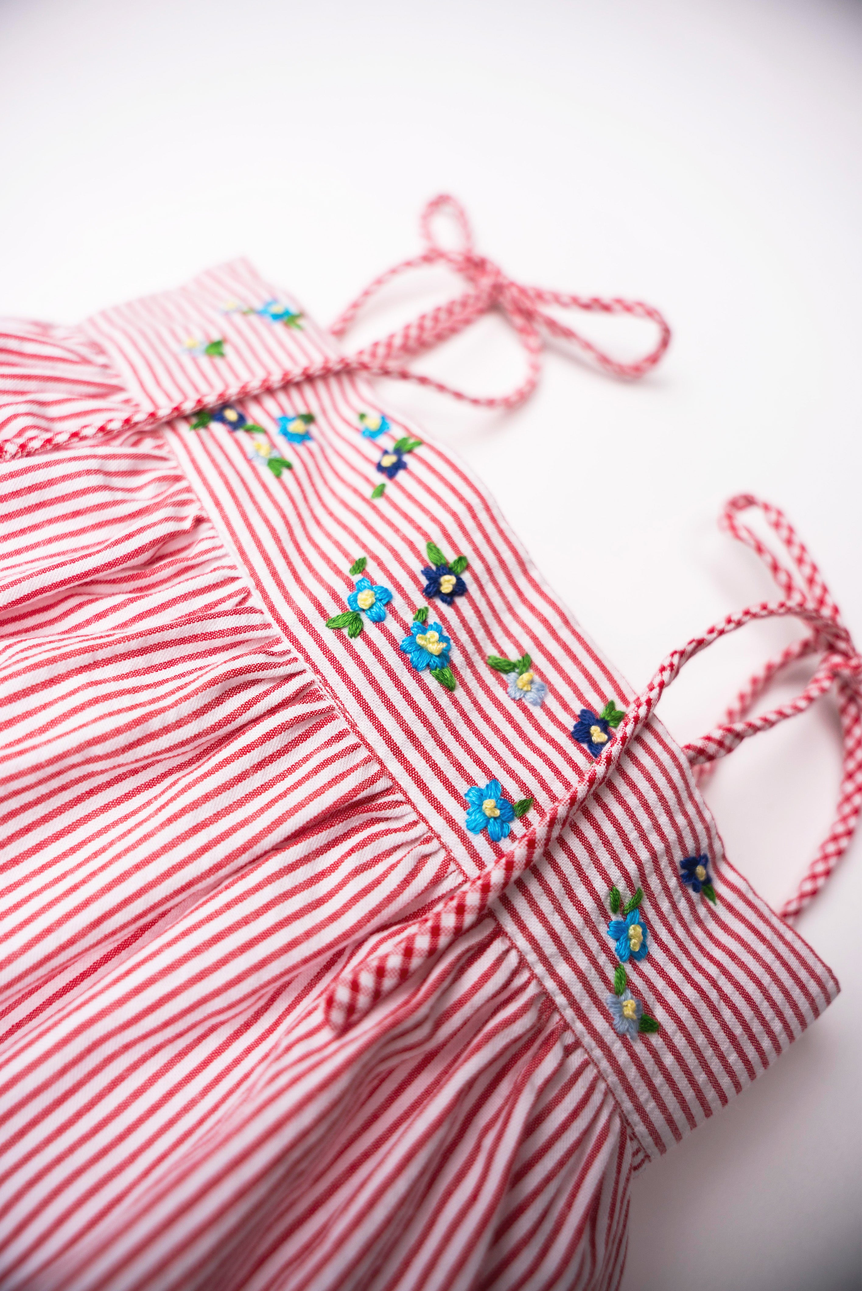 Detalhe das flores azuis bordadas à mão e das alças com efeito xadrez no Vestido Flora vermelho listrado.