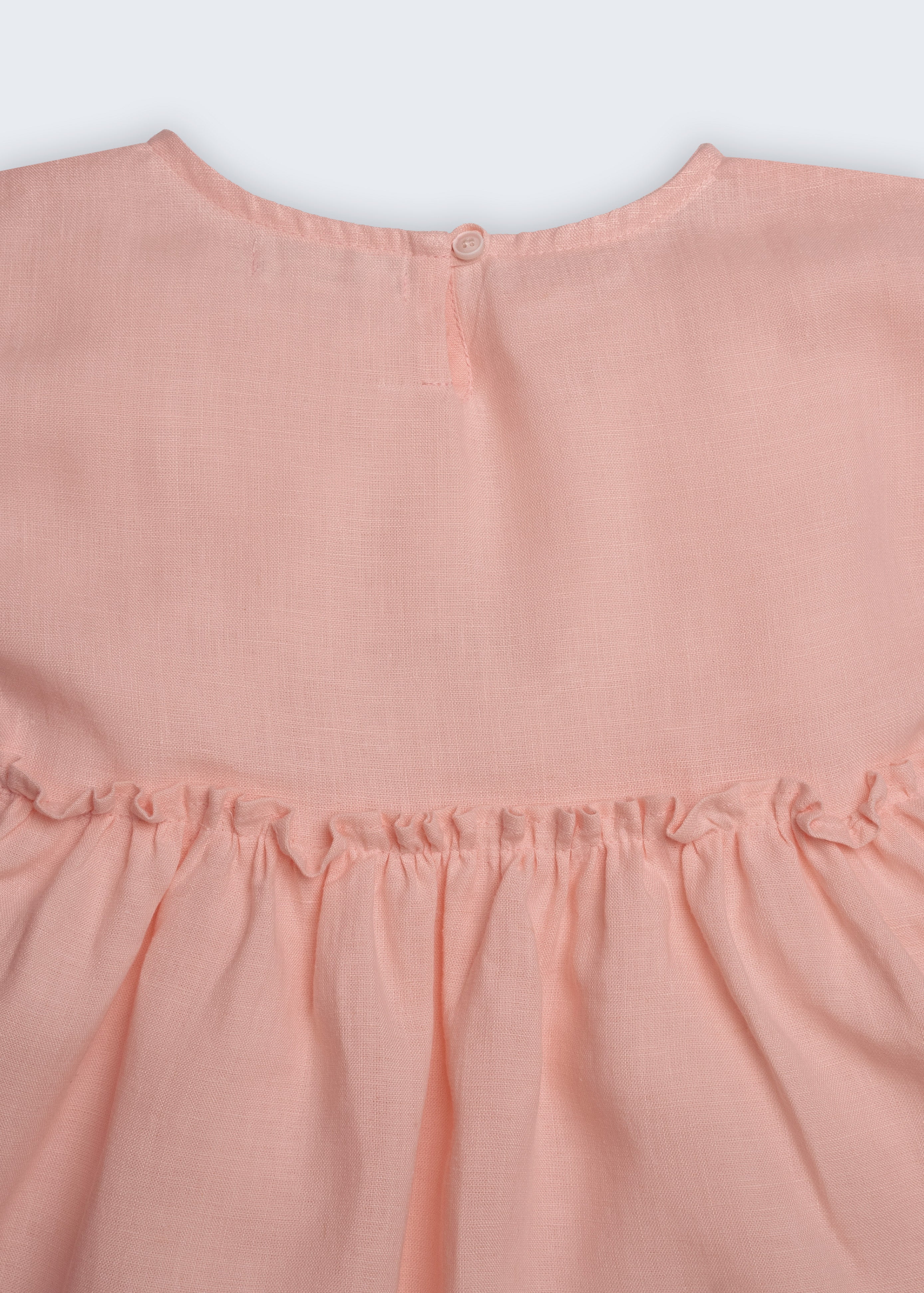 Vestido Pietra em puro linho rosa claro, com mangas e saia com babado, visto de costas em detalhe.