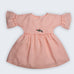 Vestido Pietra em puro linho rosa claro, com mangas e saia com babado e bordado manual de porquinhos, visto de frente.