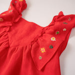 Close do bordado manual de estrelas nas alças de vestido infantil vermelho em linho.