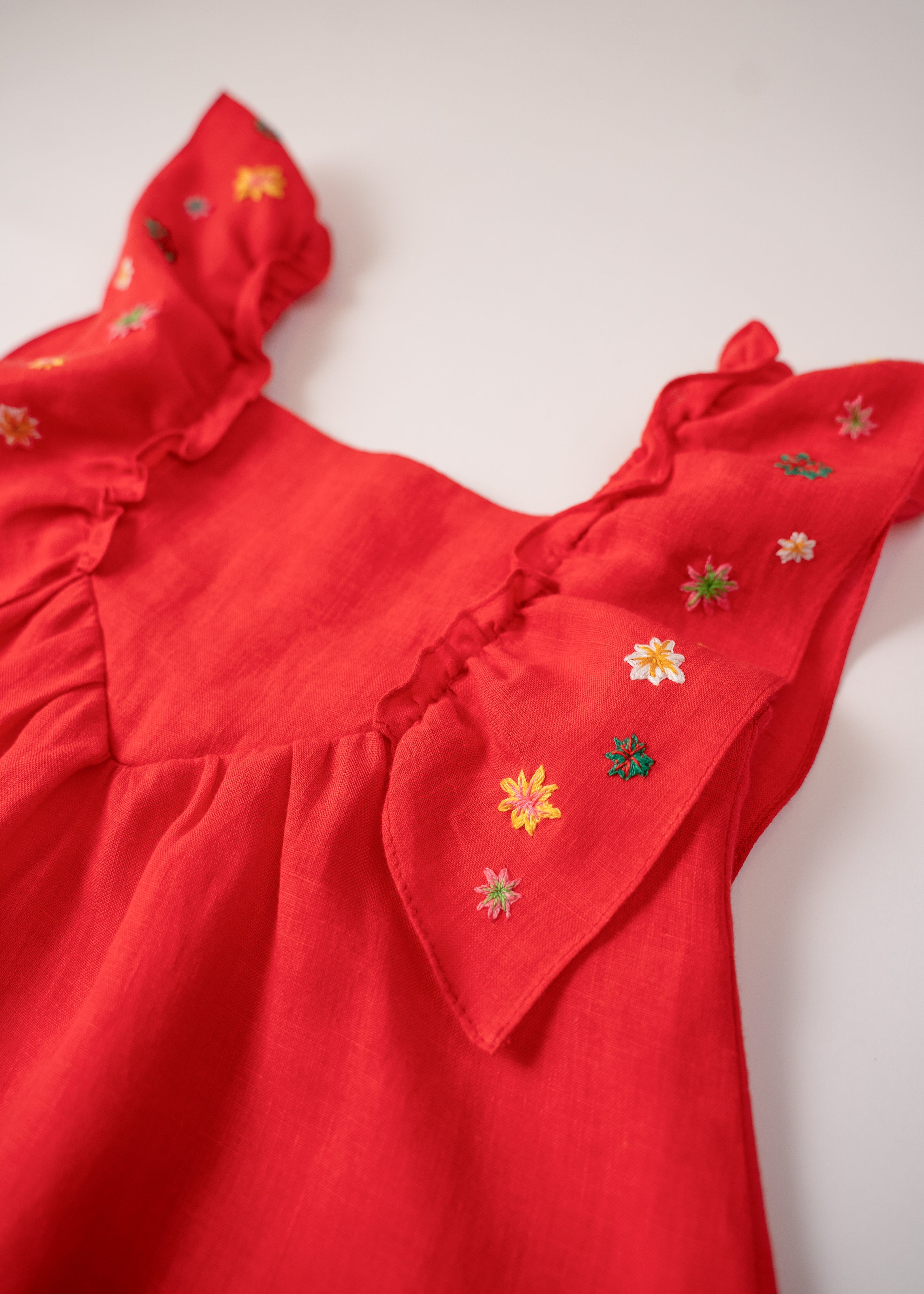 Close do bordado manual de estrelas nas alças de vestido infantil vermelho em linho.