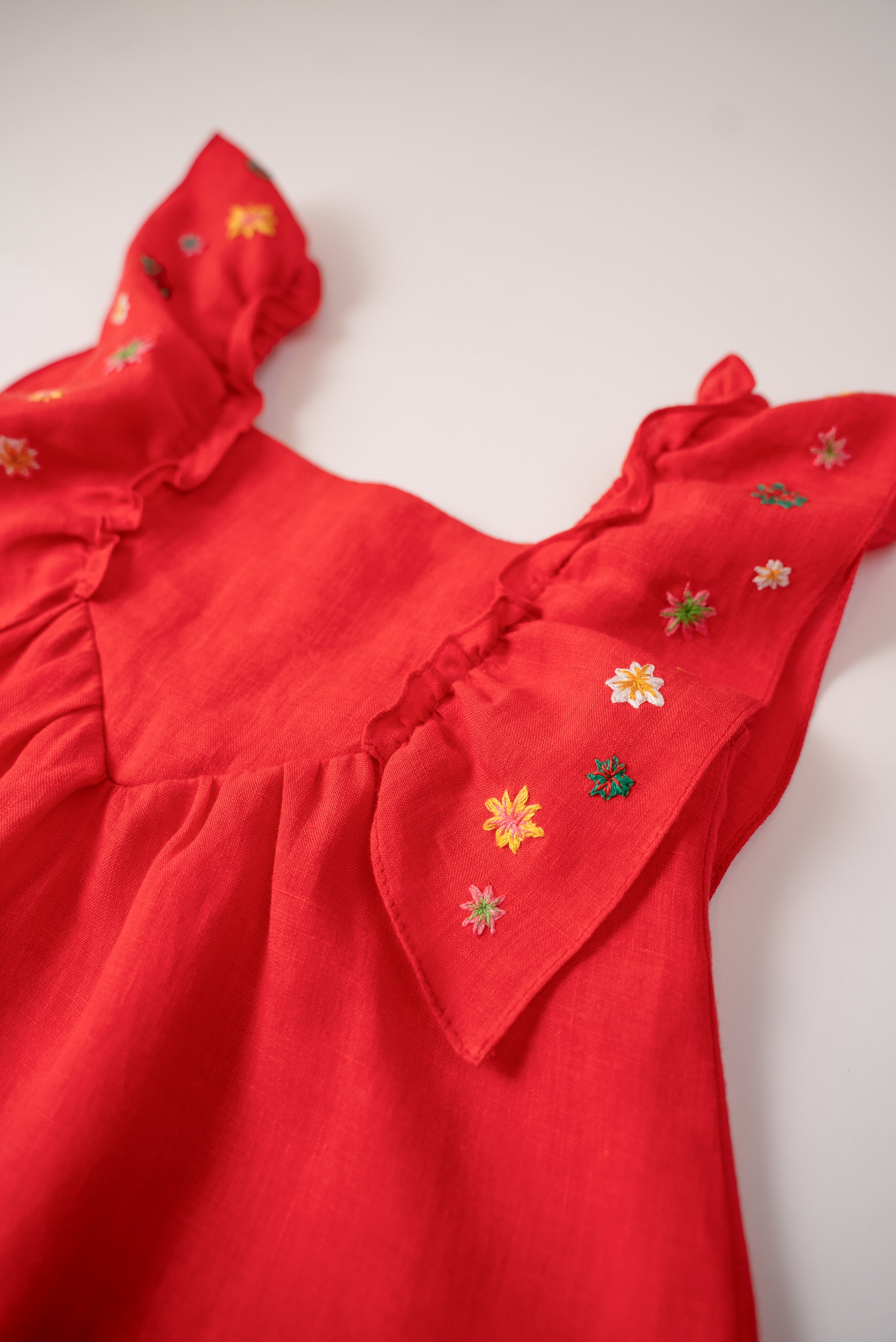Close do bordado manual de estrelas nas alças de vestido infantil vermelho em linho.