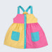 Vestido infantil color block em amarelo, rosa pink e azul turquesa para meninas, com bolsos frontais e alças retas, visto de frente.