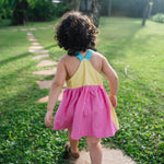 Detalhe das costas cavadas do vestido infantil em viscose Ecovero™ com alças retas azul turquesa, pala amarela e saia franzida em rosa pink. 