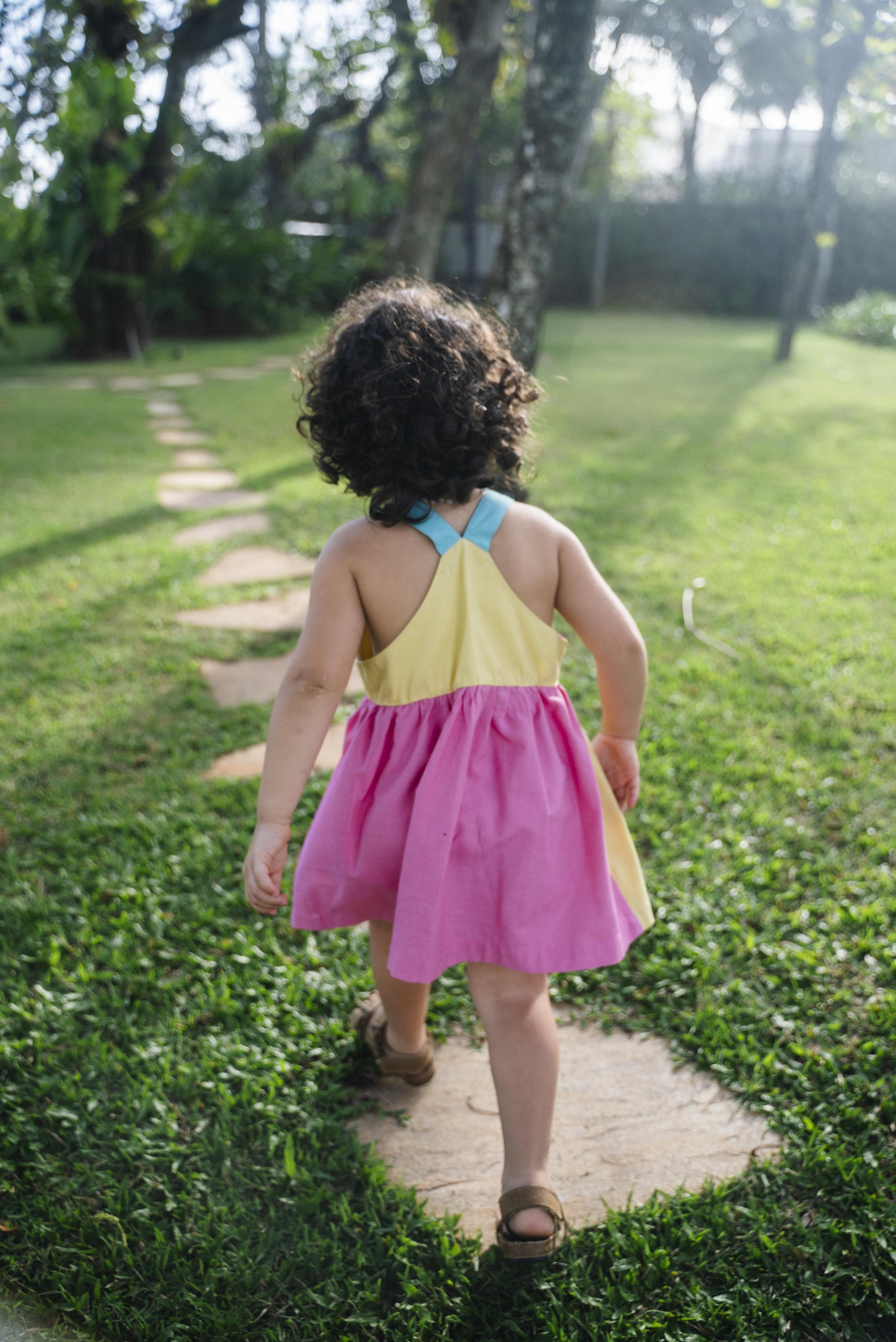 Detalhe das costas cavadas do vestido infantil em viscose Ecovero™ com alças retas azul turquesa, pala amarela e saia franzida em rosa pink. 