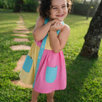 Bebê menina usando vestido infantil color block em viscose Ecovero™ e algodão BCI com bolsos e carcela azuis.
