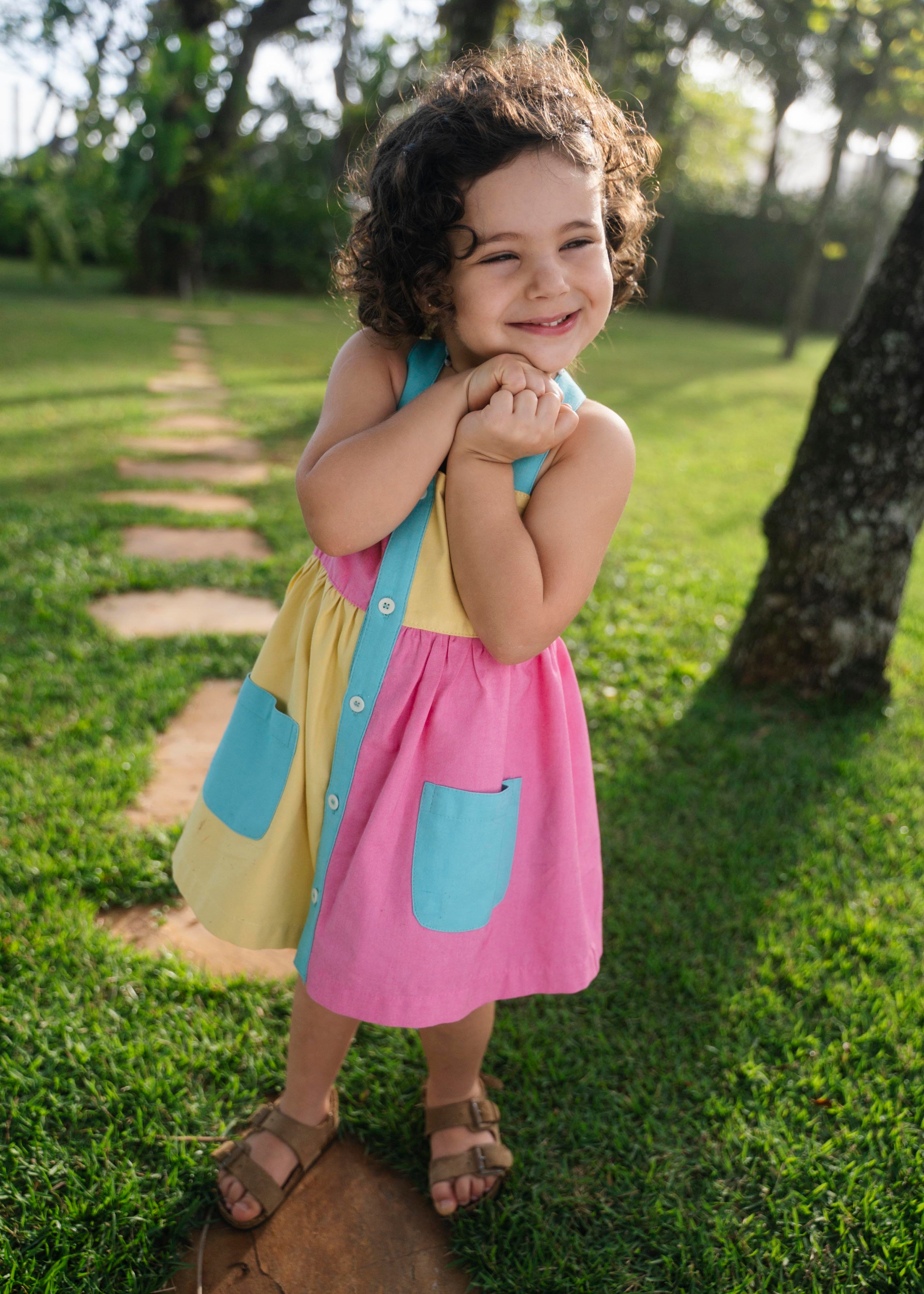 Bebê menina usando vestido infantil color block em viscose Ecovero™ e algodão BCI com bolsos e carcela azuis.