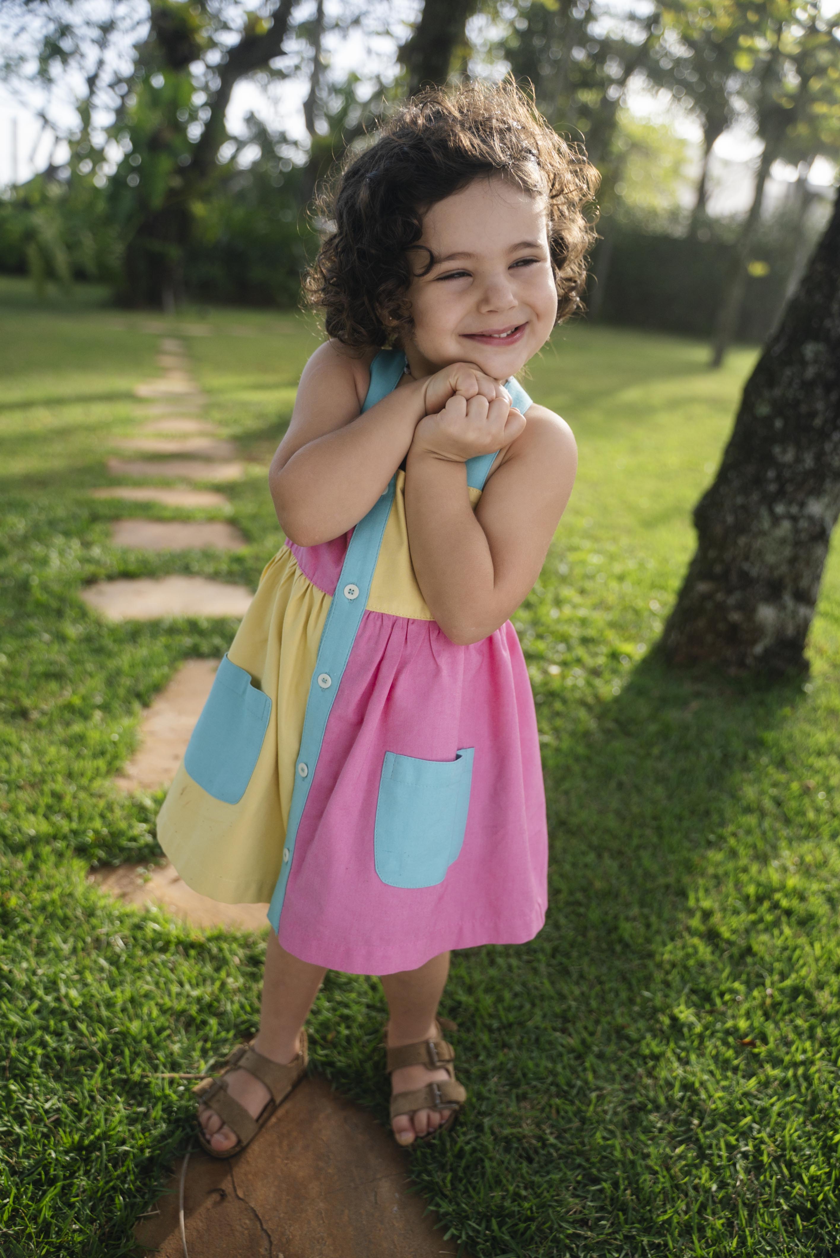 Bebê menina usando vestido infantil color block em viscose Ecovero™ e algodão BCI com bolsos e carcela azuis.